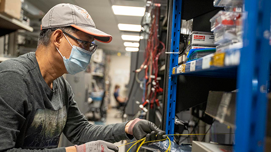 Man with a mask on, working on a set of equipment on a rack 