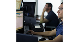Two men working on multiple computer monitors in an office setting.