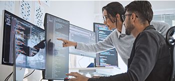 Two people collaborate at a workstation with multiple screens