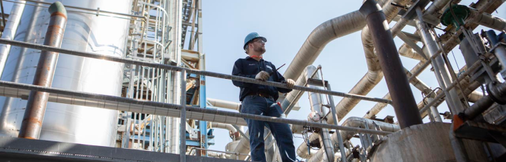 Worker stands in an oil and gas facility holding a MOTOTRBO radio. 
